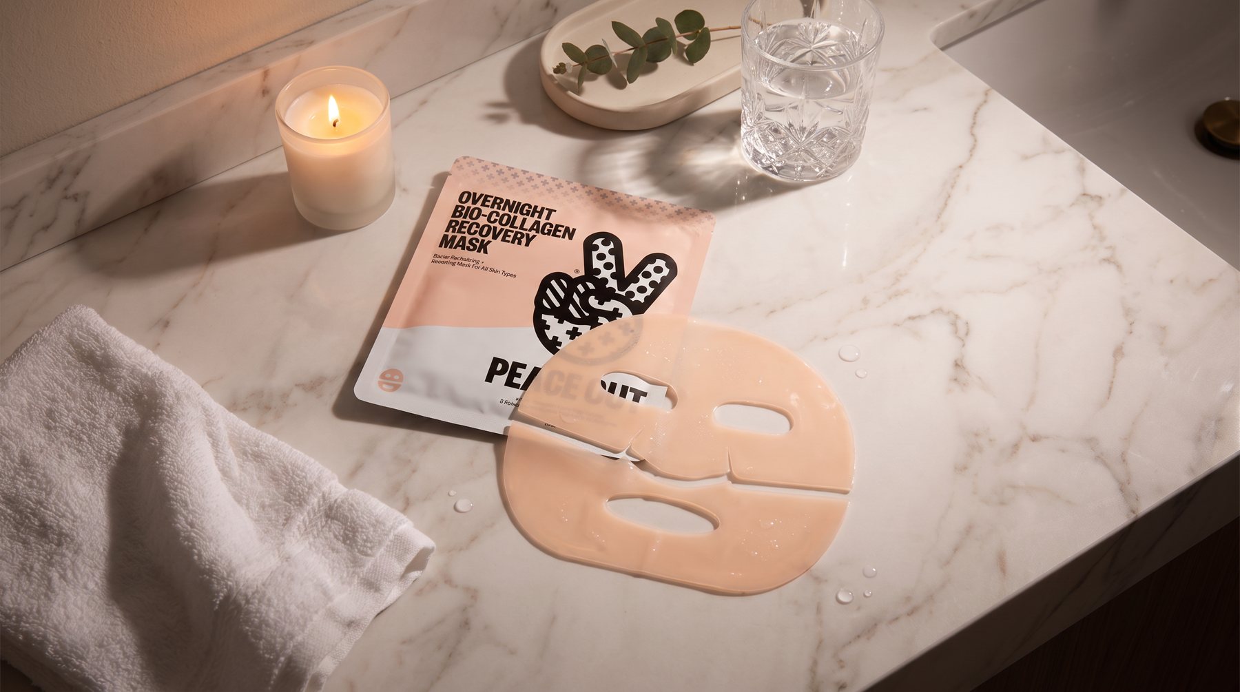 Recovery Mask pouch and hydrogel mask on marble with a candle, towel and water glass